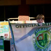 Student holds up "Official Michigan Green School" flag in front of school posters